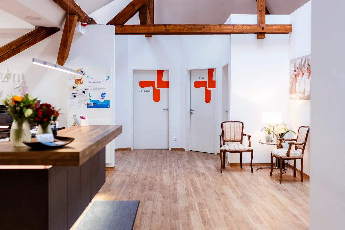Empfangsbereich der Praxisklinik mit Tresen, Blumen und den orangefarbenen Logo-Glastüren