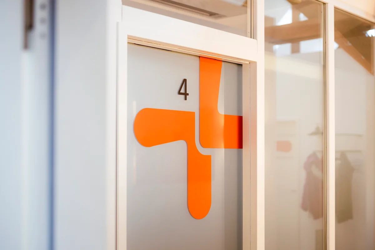 Glastür mit orangefarbenem Praxislogo und Zimmernummer